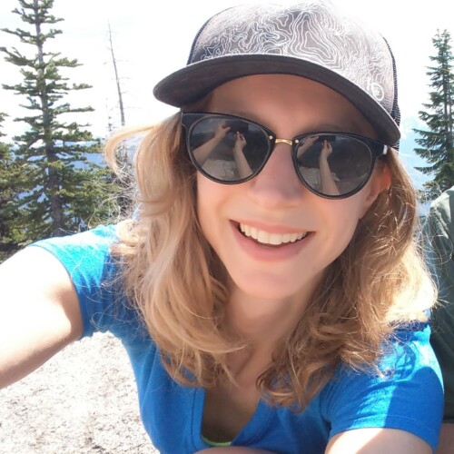 A headshot of Melani wearing sunglasses and a hat while on a hike.